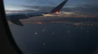 Vy från flygplansfönster över Hormuzsundet med fartygsljus i vattnet och kustljus i horisonten