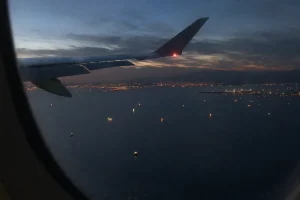 Vy från flygplansfönster över Hormuzsundet med fartygsljus i vattnet och kustljus i horisonten