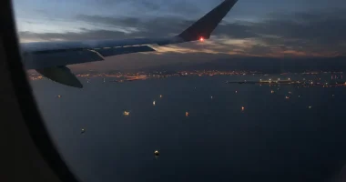 Vy från flygplansfönster över Hormuzsundet med fartygsljus i vattnet och kustljus i horisonten